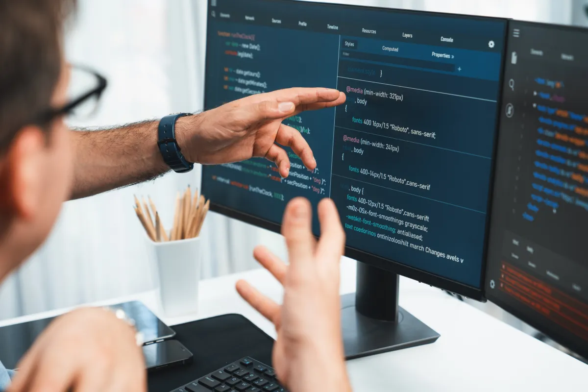 Persoon wijst naar code op computerscherm tijdens softwareontwikkeling