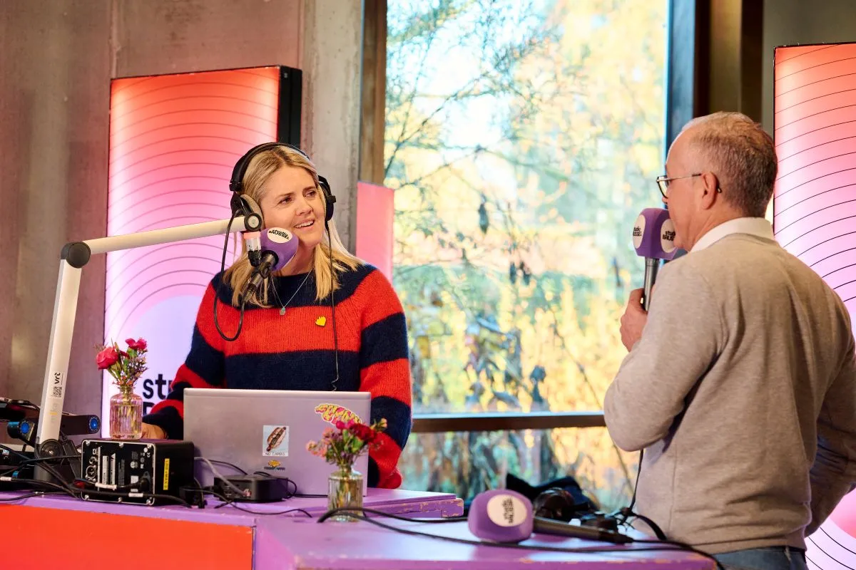 Twee mensen in een radiostudio in gesprek met microfoons en koptelefoons tijdens een live opname