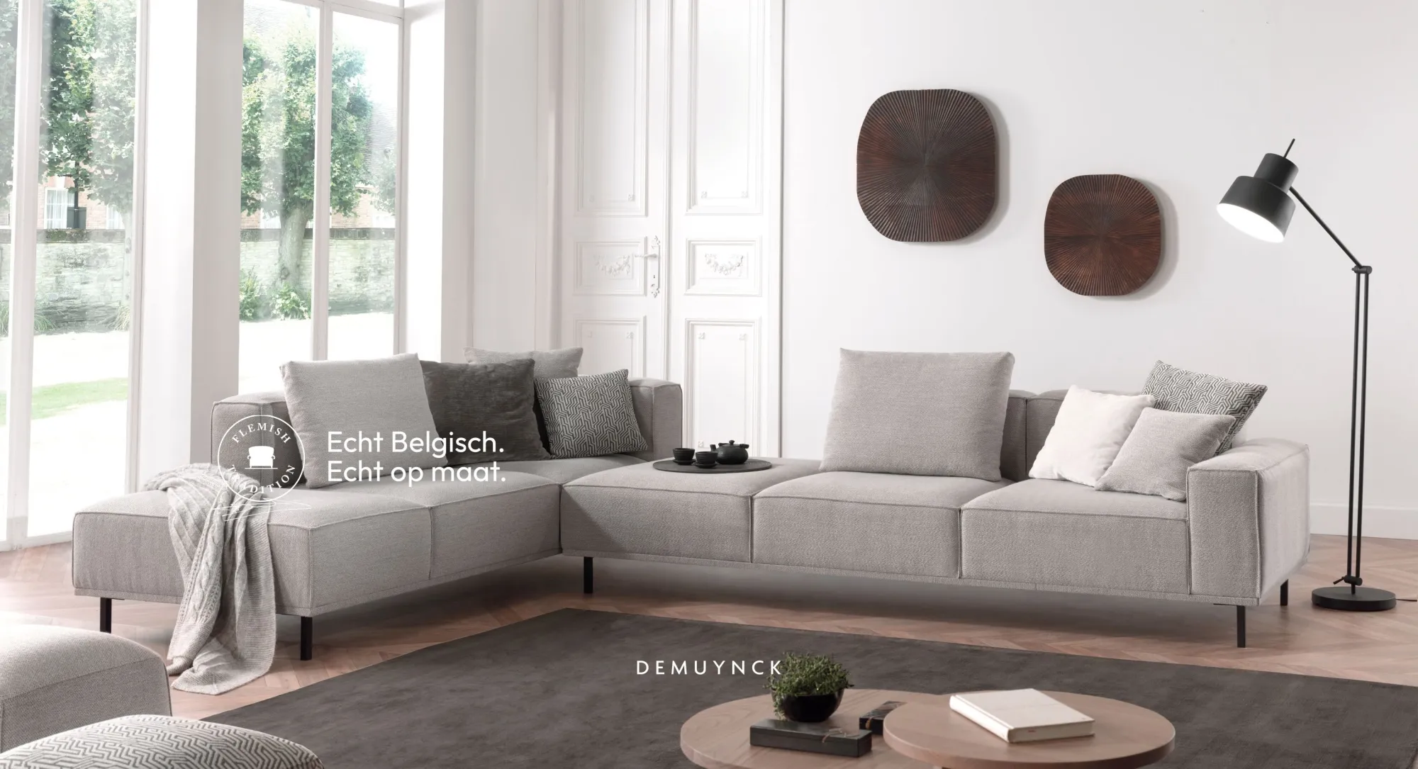 Spacious custom grey corner sofa by Demuynck Furniture Wevelgem in a bright living room, featuring the Flemish Tradition quality label